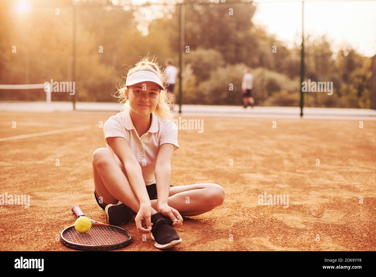 Repose sur le sol. Une jeune joueuse de tennis en vêtements de sport se trouve sur le court à l'extérieur Banque D'Images