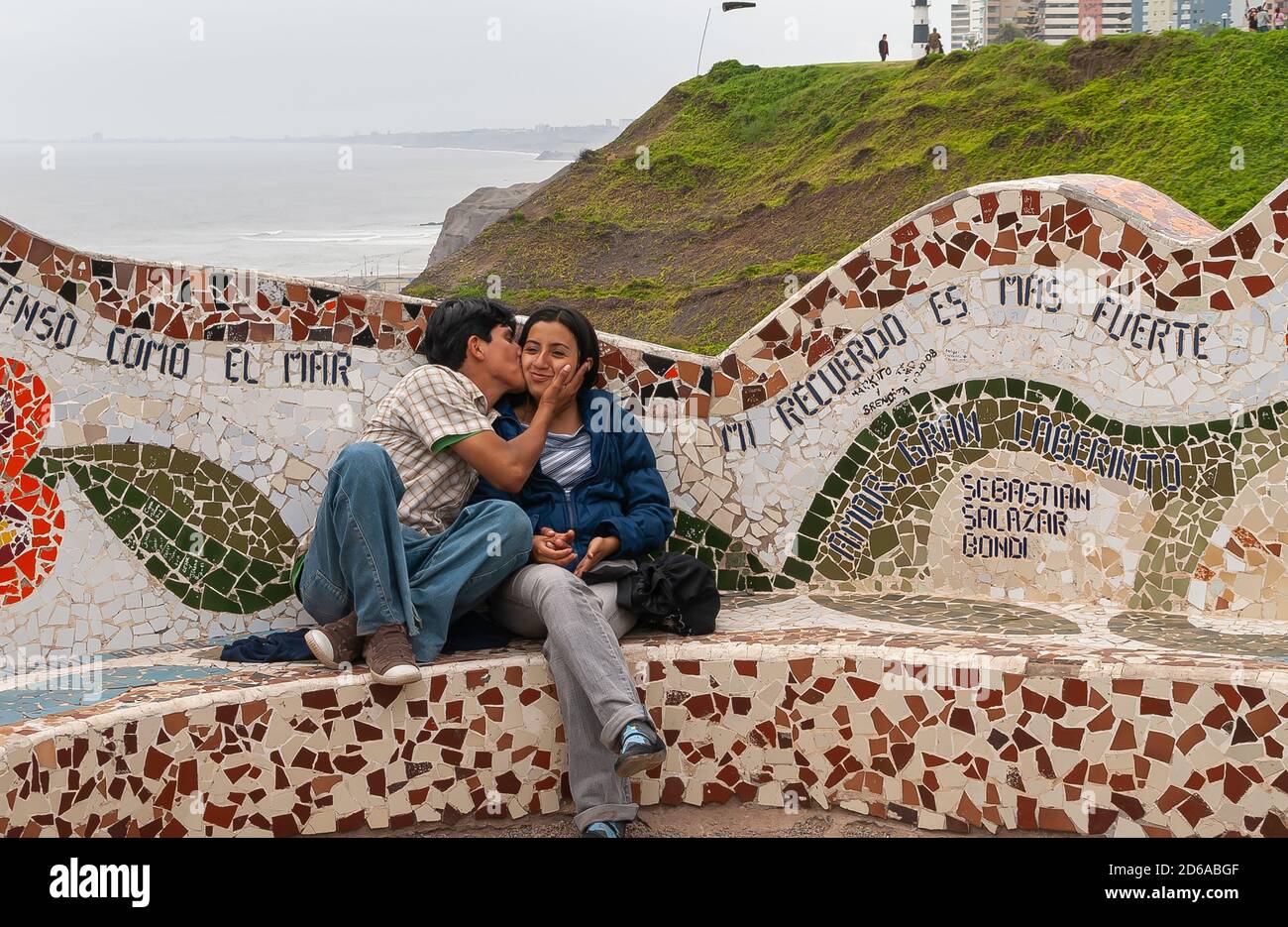 Miraflores, Pérou - 4 décembre 2008 : Parque del Amor, Love Park. Jeune couple embrassant sur un banc en mosaïque avec océan et falaise verte en arrière-plan. Banque D'Images
