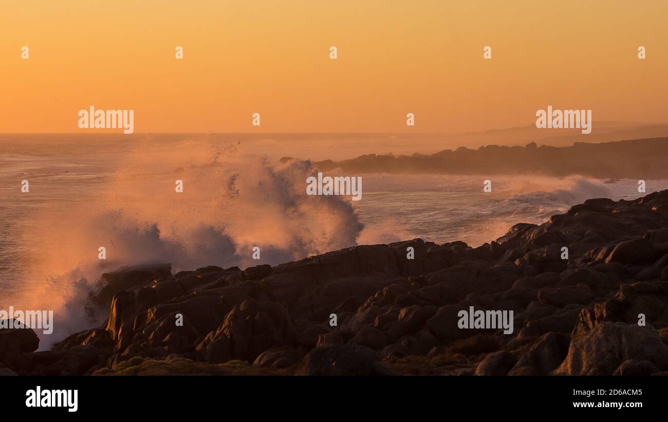 Vagues se brisant avec un jet le long de la côte ouest des Rocheuses d'Afrique du Sud, pendant le coucher du soleil colorant tout une couleur orange rose Banque D'Images