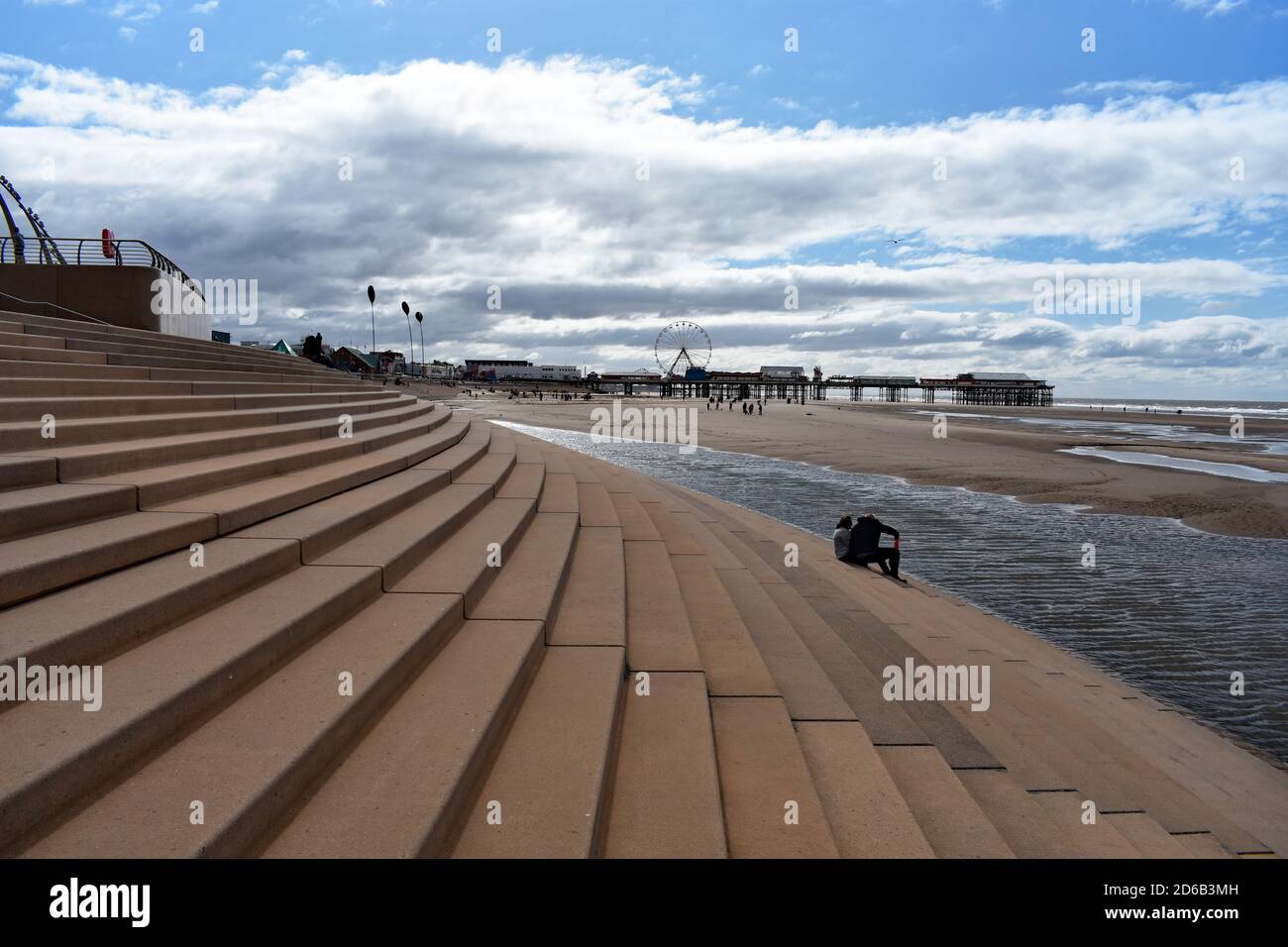 Un couple s'assoit sur des marches qui mènent de la promenade à la plage de Blackpool, en Angleterre. Vous pourrez voir Central Pier qui mène à la mer d'Irlande. Banque D'Images