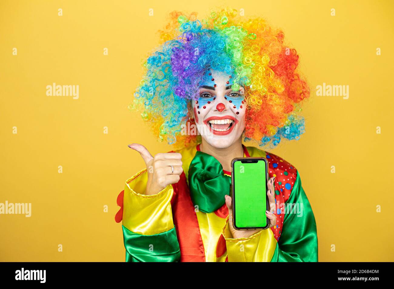 Clown debout sur fond jaune insolé jaune souriant, montrant le téléphone et pointant sur le côté Banque D'Images