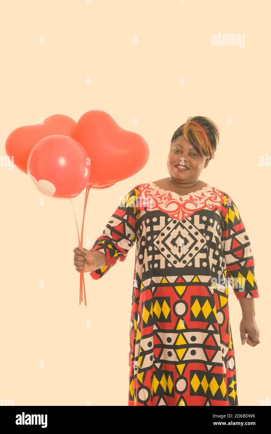 Photo studio d'une femme africaine noire et grasse souriante tenue de ballons rouges avec enseigne en forme de coeur Banque D'Images