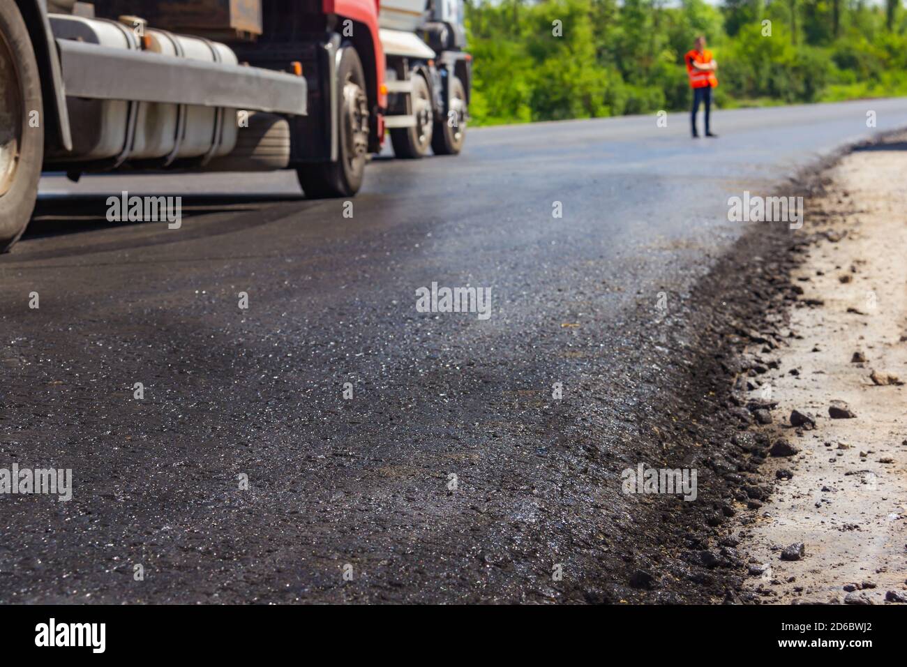 Gros plan d'une nouvelle route et d'une nouvelle machine à revêtement récemment pavée avec des constructeurs en uniforme à l'arrière-plan. Banque D'Images