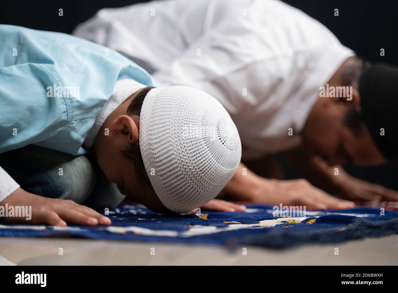 Le père et le fils musulmans priant ou exécutant Salah tout en étant assis sur le tapis de prière et en touchant la tête à la mihrab ou à la mosquée imprimée sur le tapis. Banque D'Images