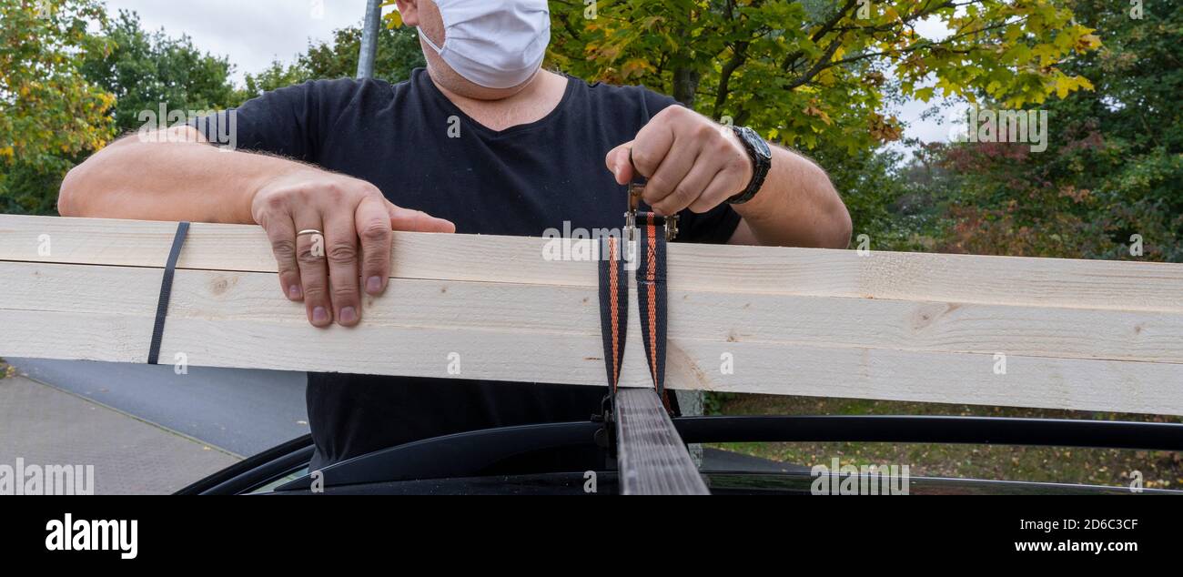 Homme d'âge moyen portant un masque de protection fixé des poutres en bois sur sa voiture. Banque D'Images