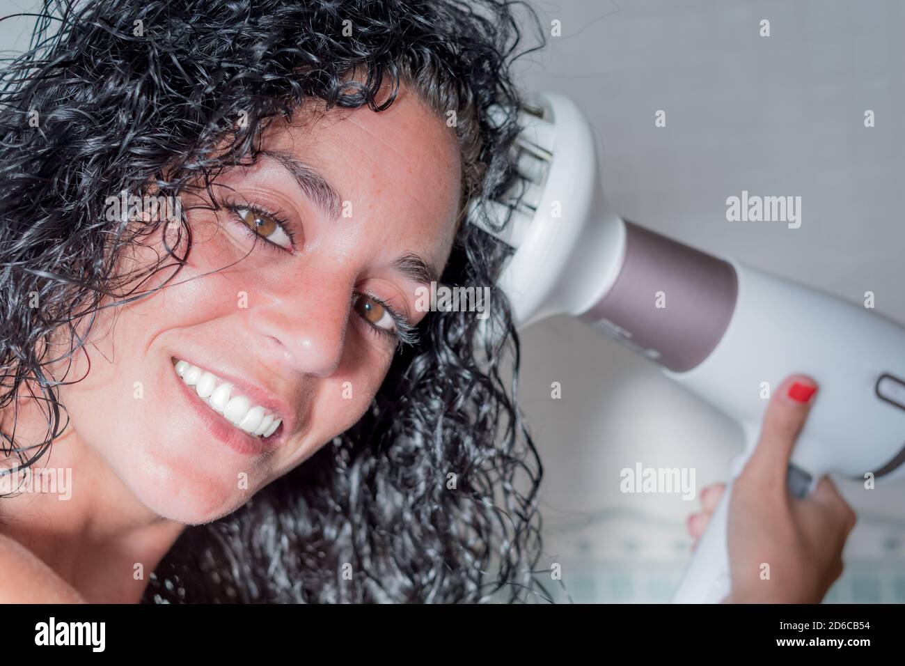 gros plan d'une femme souriante qui se curde ses cheveux avec un sèche-cheveux doté d'une brosse spéciale pour boucler ses cheveux. sèche-cheveux avec diffuseur. concept soin et beauté. Banque D'Images