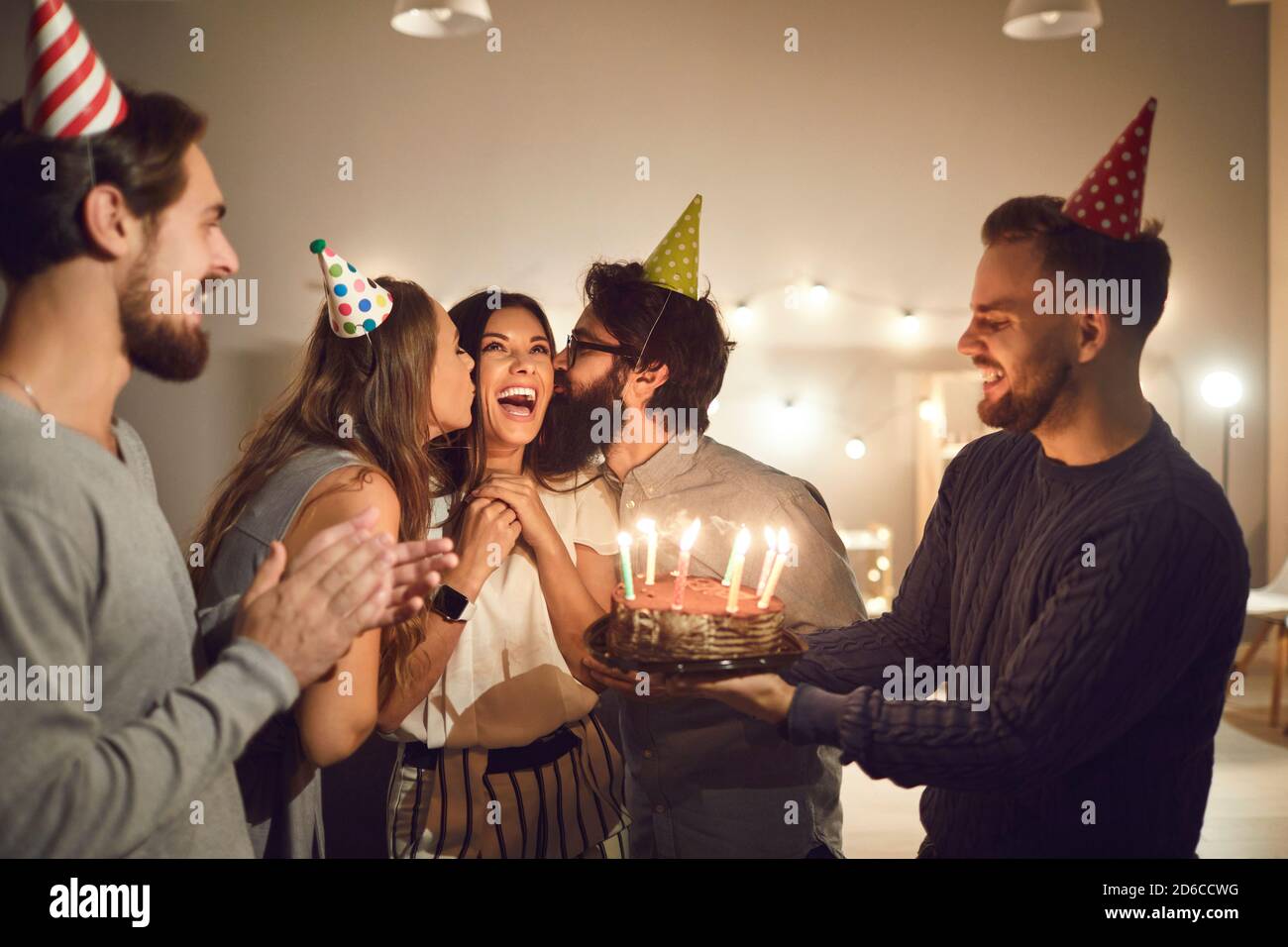 Des jeunes heureux embrassant leur ami sur les joues et donnant elle a un gâteau de fête d'anniversaire avec des bougies Banque D'Images