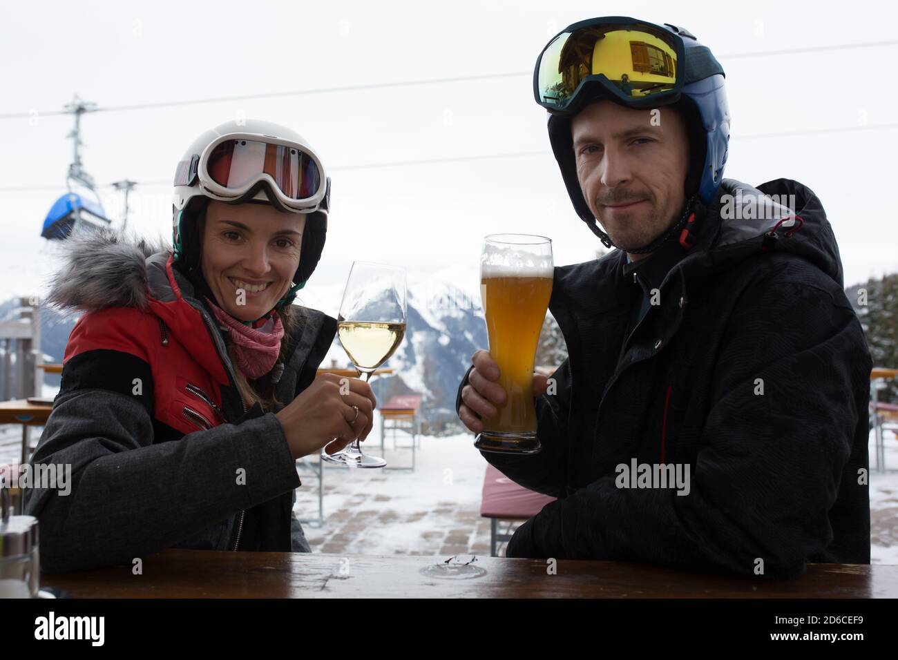 Femme et homme, mari et femme, buvant de la bière et du vin dans un restaurant sur une piste de ski pendant une pause de ski dans l'après-midi, par une journée nuageuse Banque D'Images