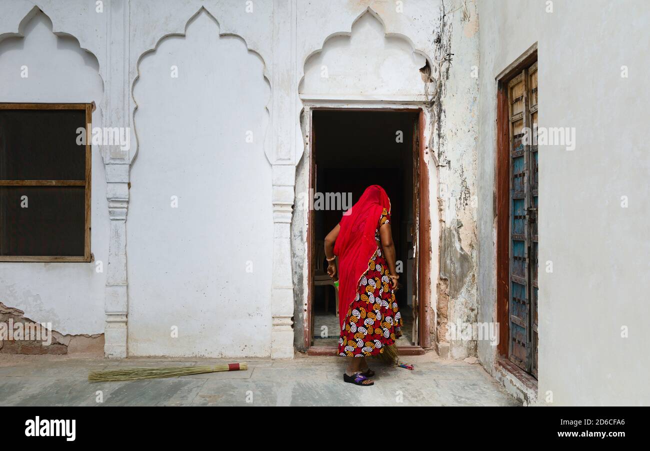 Femme, dans les vêtements traditionnels, avec dos à la caméra balayer la véranda extérieure de la maison à Pushkar, Rajasthan, Inde. Banque D'Images