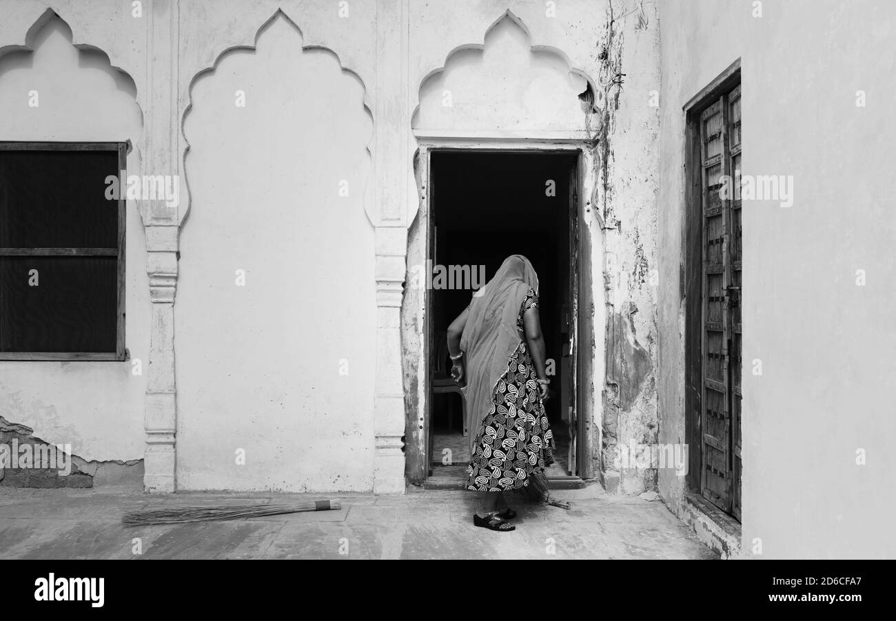 Femme, dans les vêtements traditionnels, avec dos à la caméra balayer la véranda extérieure de la maison à Pushkar, Rajasthan, Inde. Banque D'Images