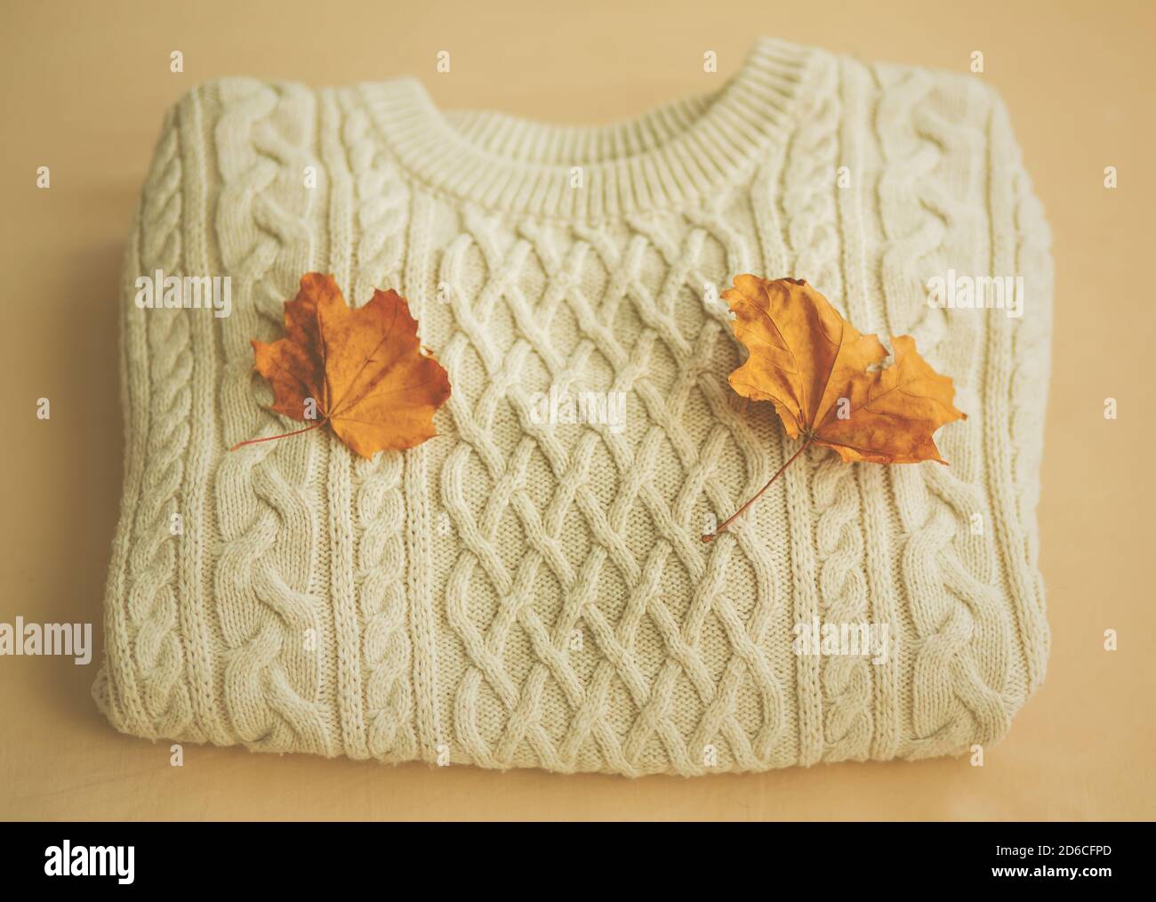 Vue de dessus d'un pull en laine blanche à motifs, sur lequel reposent deux feuilles d'érable sèches, sur un fond beige. Automne. Jours froids. Banque D'Images