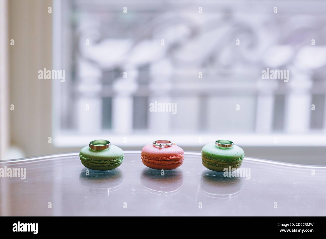 Gros plan sur des anneaux de mariage posés sur des macarons doux sur fond de fenêtre. Lumière du jour. Banque D'Images