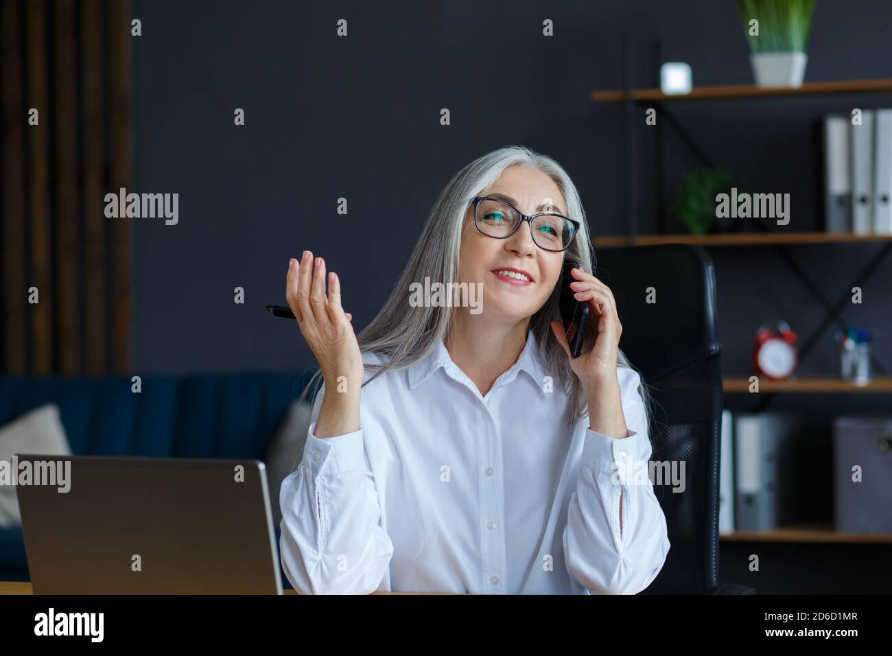 Femme d'affaires souriante, sénior et aux cheveux gris, qui parle au téléphone au bureau. Portrait d'affaires d'une belle femme mature portant des lunettes Banque D'Images