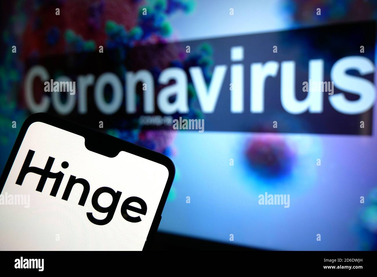 Le logo de l'application Hinge datant est affiché sur un téléphone portable avec un modèle d'illustration du coronavirus affiché sur un moniteur en arrière-plan. Banque D'Images