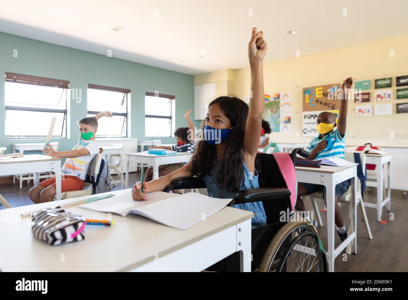 Désactiver la fille portant un masque facial levant sa main pendant qu'elle est assise en fauteuil roulant en classe Banque D'Images