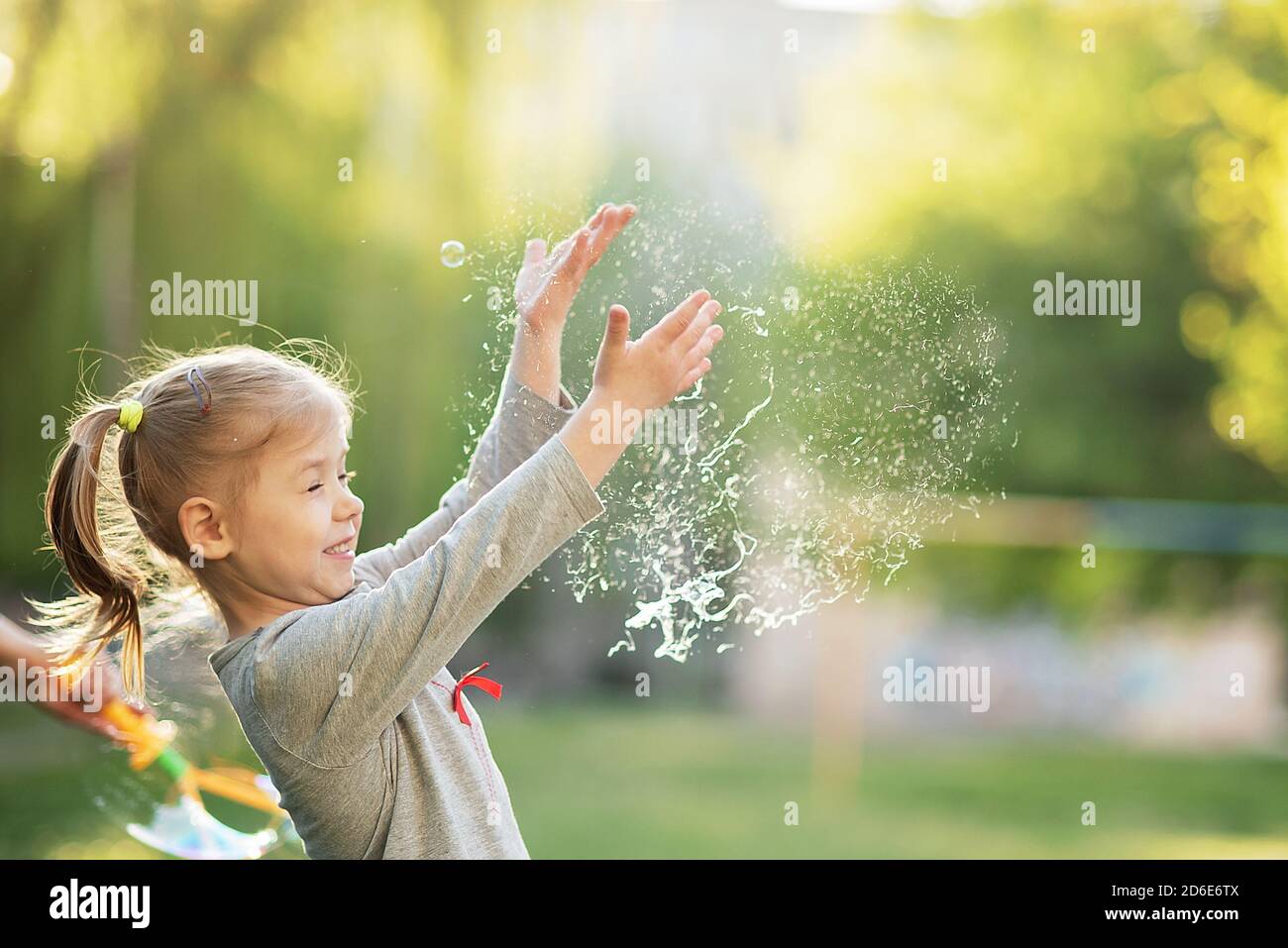 Un enfant heureux de 5 ans éclate des bulles de savon dans le jardin. Vacances d'été dans la nature. Portrait émotionnel de la bonne et active petite belle fille débordant Banque D'Images