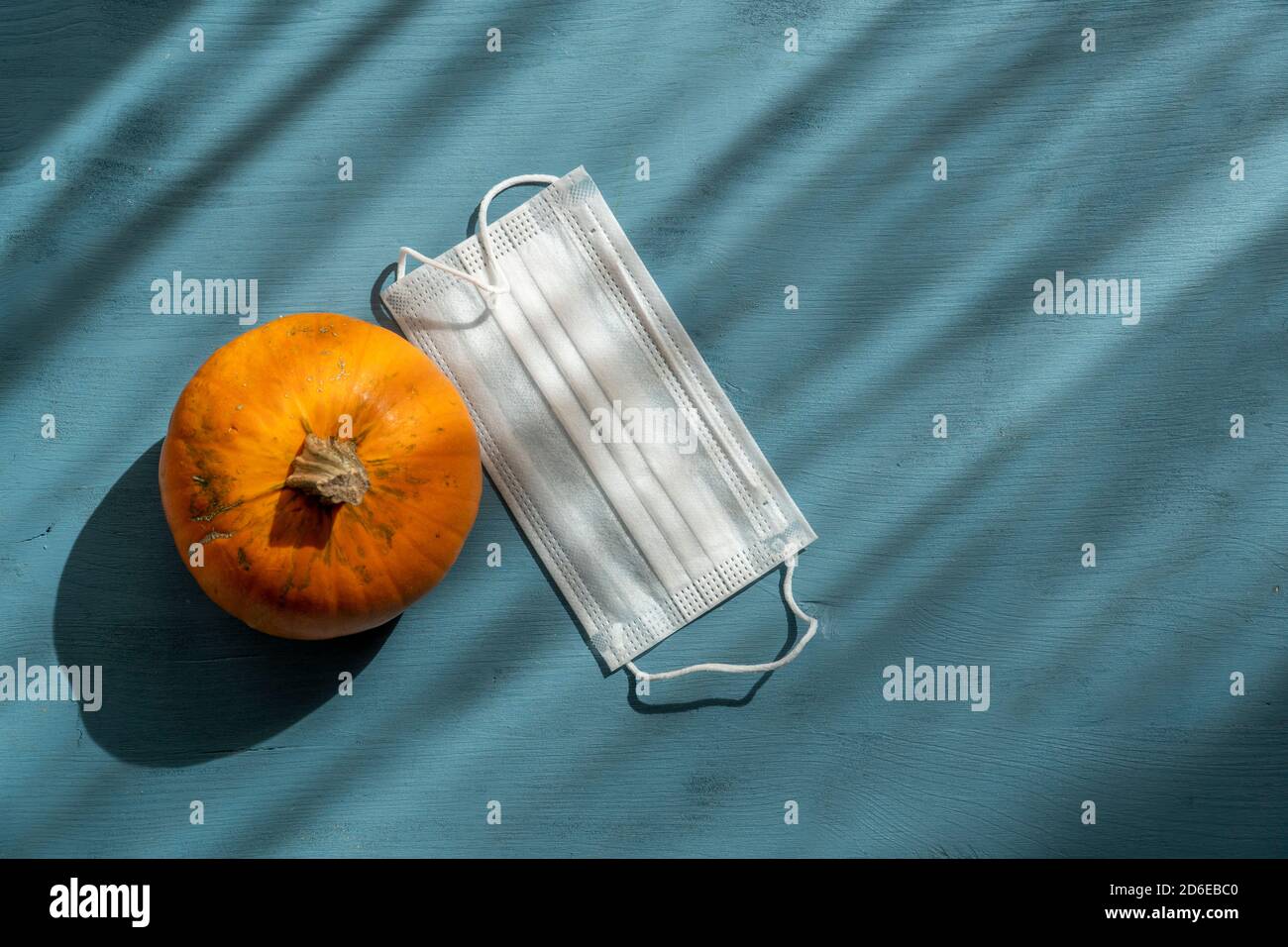 Citrouille d'Halloween et masque facial pour le virus corona sur fond bleu avec éclairage spectaculaire. Banque D'Images