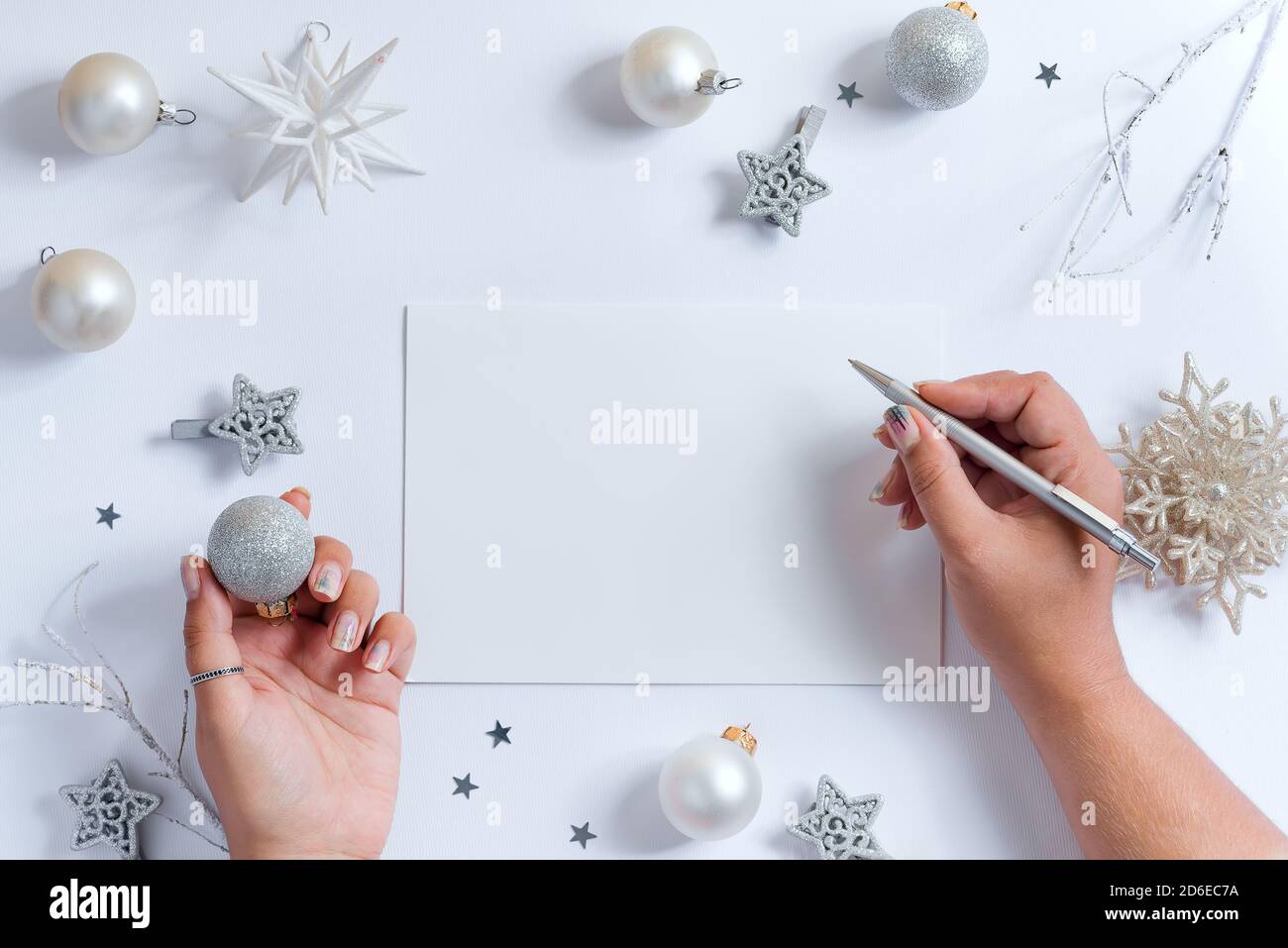 Les mains des femmes écrivent la lettre au Père Noël au-dessus du fond de Noël décoré avec de belles étoiles brillantes et des boules de couleurs blanc et argent, copie Banque D'Images