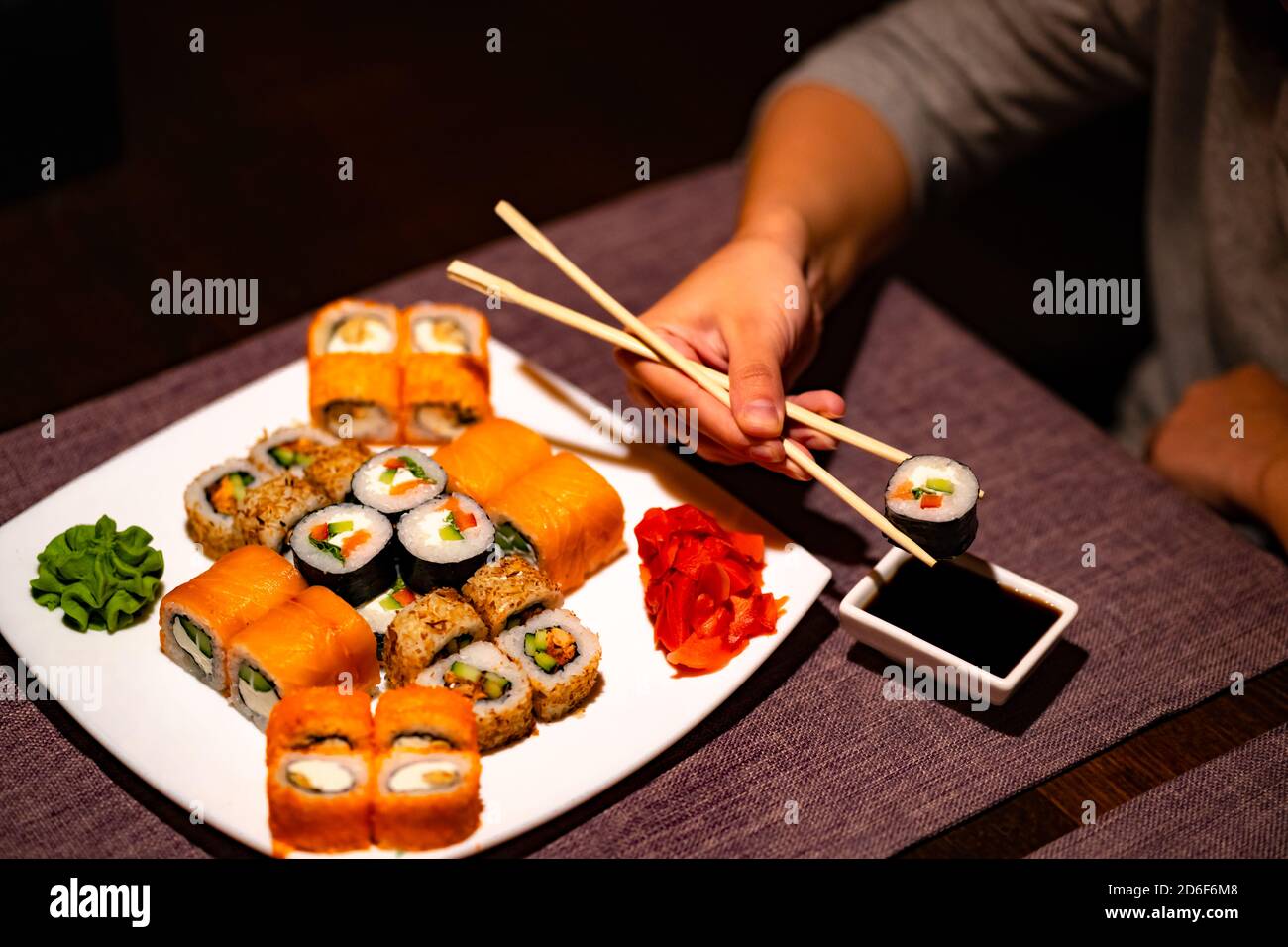 Personne mangeant des sushis avec des baguettes au restaurant. Crop anonyme personne avec des baguettes mangeant divers types de rouleaux de sushi servis avec wasabi et Banque D'Images