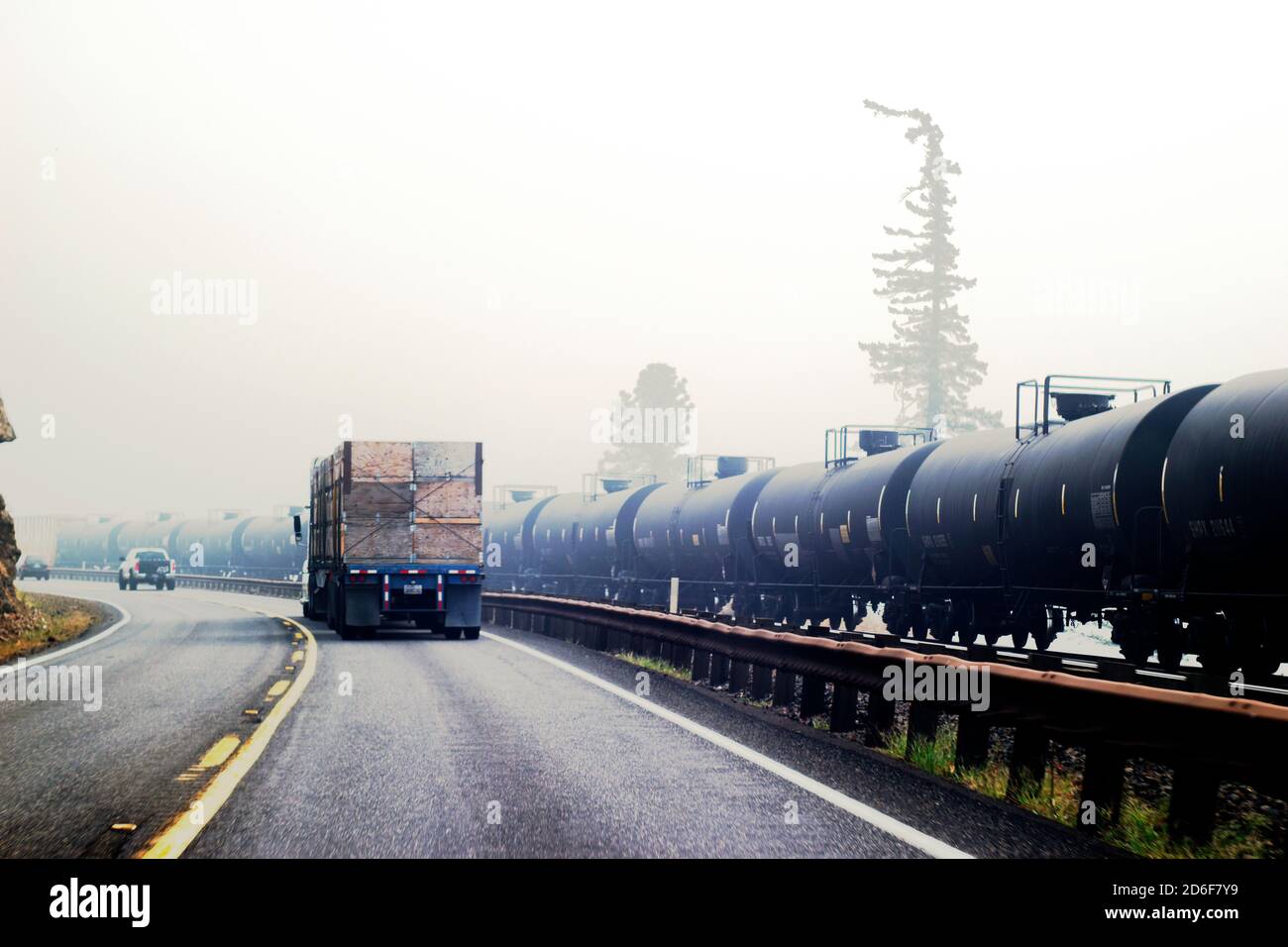 Fumée de feu de forêt et circulation routière à côté de voitures de chemin de fer transportant huile Banque D'Images