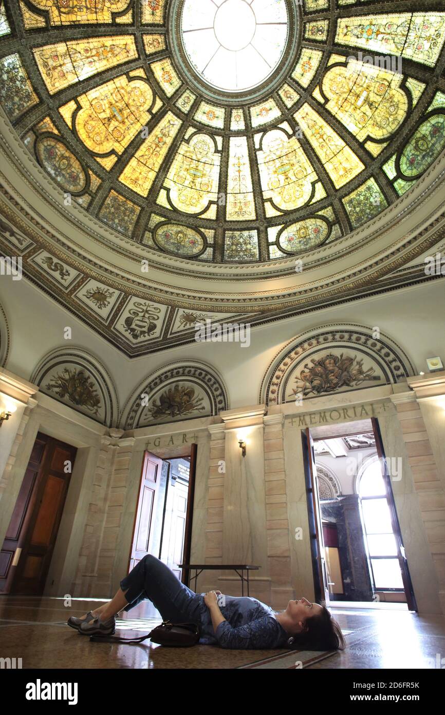 Une femme couchée sur le sol et regardant le Tiffany Dome, au Chicago Cultural Center à Chicago, Illinois. Banque D'Images