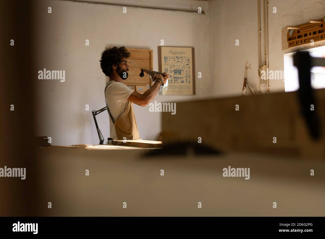 Homme hispanique travaillant comme menuisier dans un petit laboratoire de bois. L'homme barbu s'est concentré sur la mise en forme d'un nouveau morceau de bois pour un mobilier de maison dans sa ca Banque D'Images