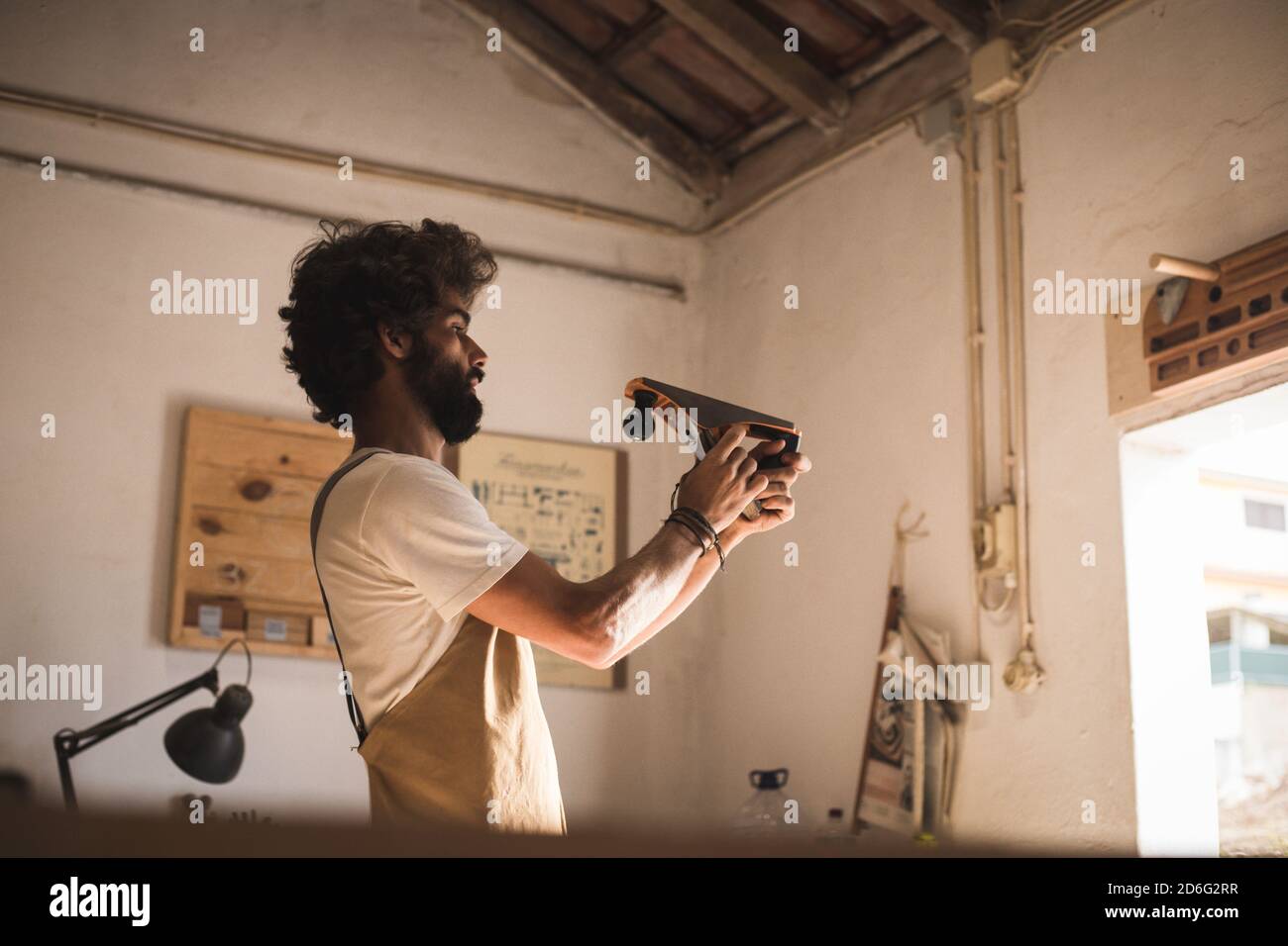 Homme hispanique travaillant comme menuisier dans un petit laboratoire de bois. L'homme barbu s'est concentré sur la mise en forme d'un nouveau morceau de bois pour un mobilier de maison dans sa ca Banque D'Images