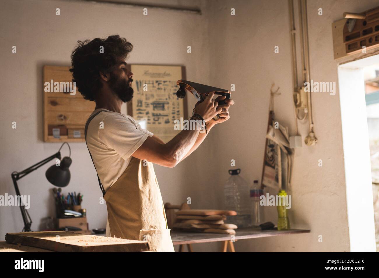 Homme hispanique travaillant comme menuisier dans un petit laboratoire de bois. L'homme barbu s'est concentré sur la mise en forme d'un nouveau morceau de bois pour un mobilier de maison dans sa ca Banque D'Images