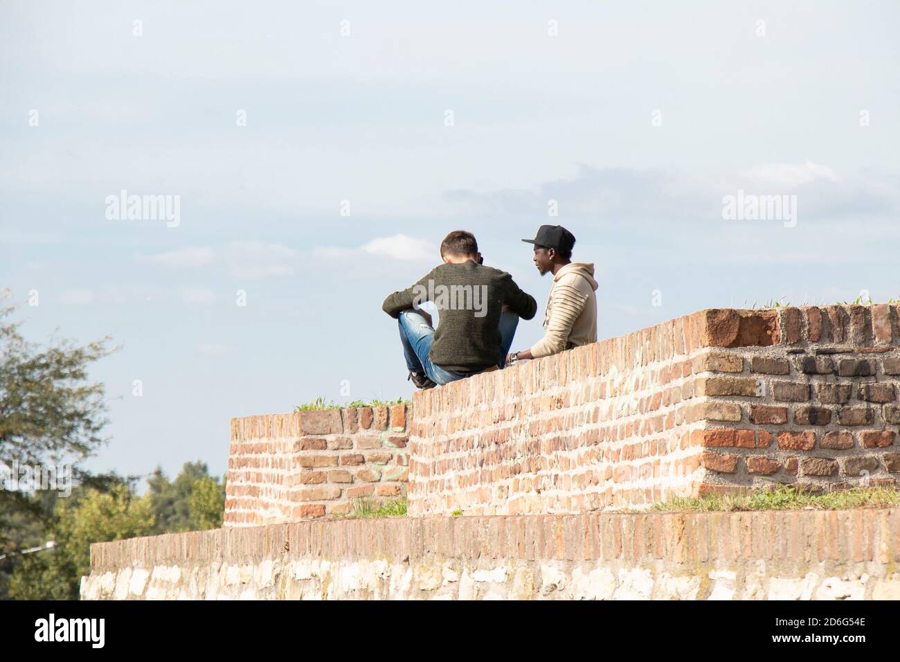 Belgrade, Serbie - 09 octobre 2020 : deux jeunes hommes assis sur le haut de la forteresse de Kalemegdan mur de briques par une journée ensoleillée, de l'arrière Banque D'Images