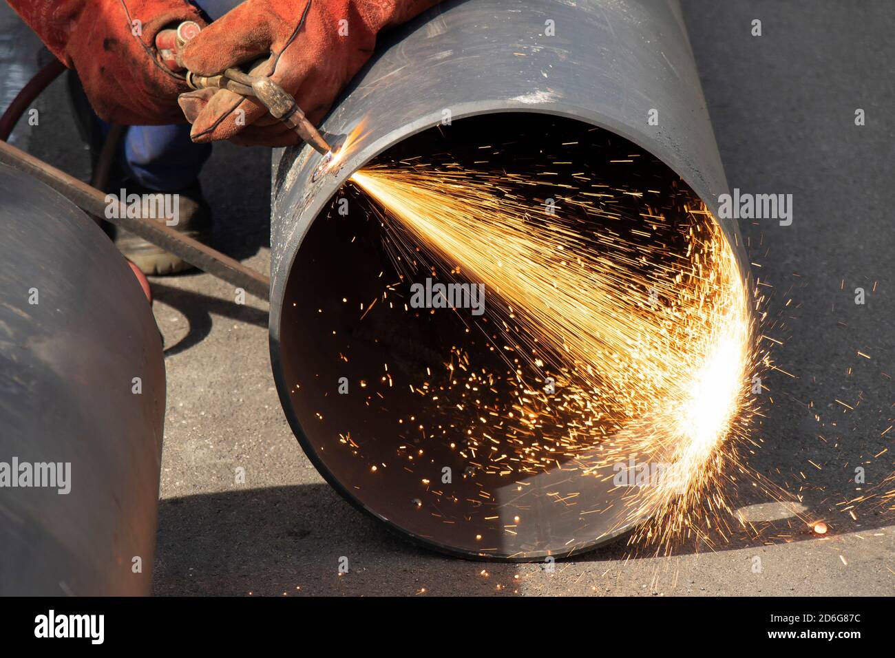 Un soudeur soudeur soudeur un tube de tuyau métallique large avec un chalumeau de découpe oxy-fuel, avec flamme et étincelles, sur un chantier de construction extérieur Banque D'Images