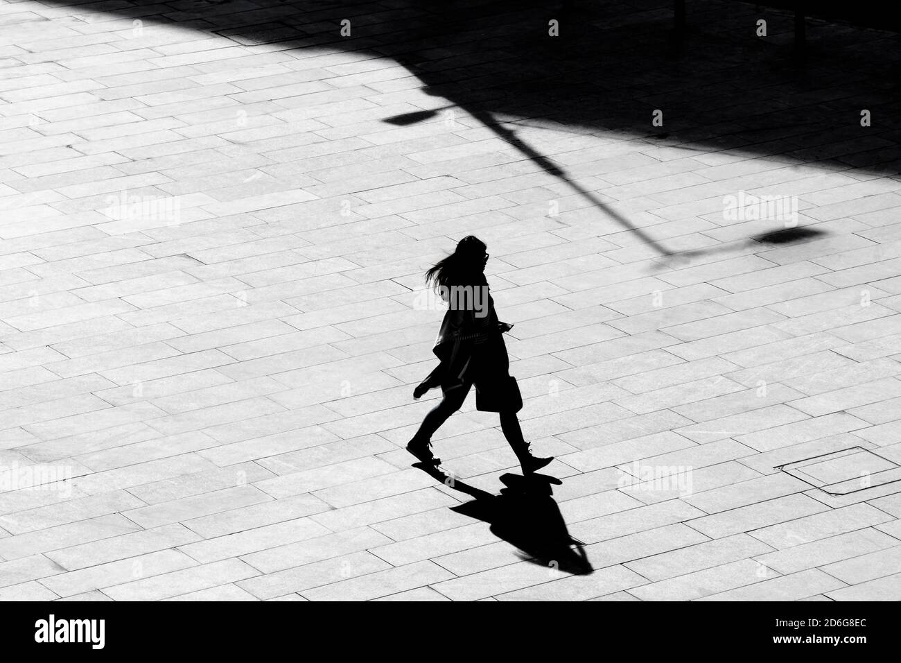 Belgrade, Serbie - 09 octobre 2020 : silhouette d'ombre d'une jeune femme marchant sur la chaussée carrée de la ville, en vue à grand angle noir et blanc Banque D'Images