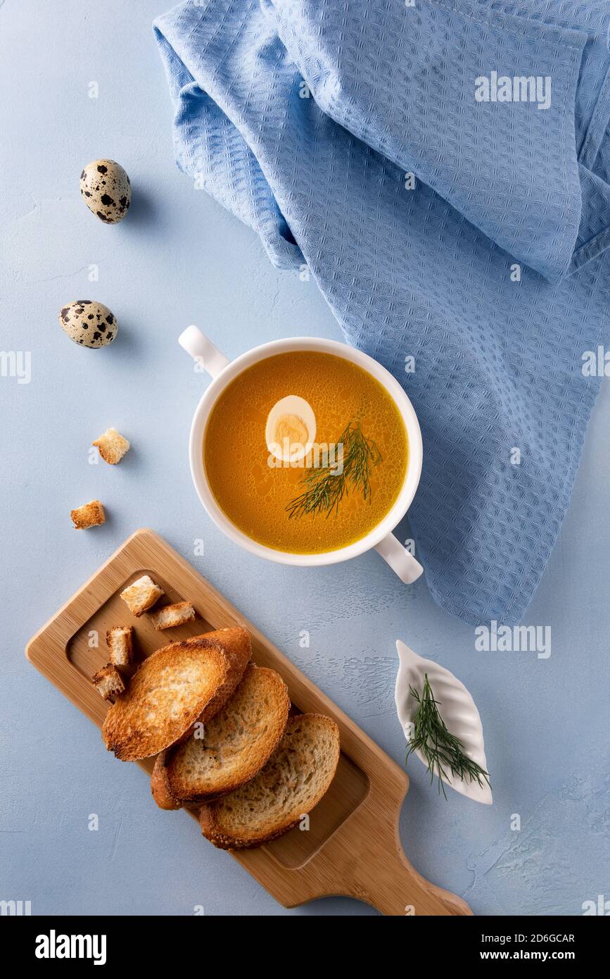 Bol à soupe blanc avec bouillon, œuf de caille et feuille de fenouil sur fond bleu. Textile de lin, œufs entiers et pain grillé. Pose à plat. Orientation verticale Banque D'Images