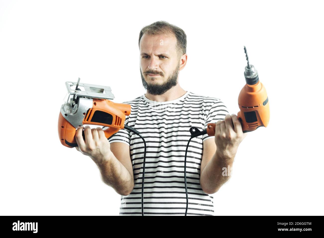 Comment choisir un outil électrique. Portrait de l'homme à main barbu tenant une perceuse orange et une scie sauteuse électrique isolée sur blanc Banque D'Images
