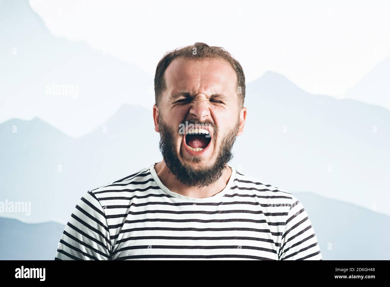 Un homme barbu hurlant dans un t-shirt rayé. Portrait émotionnel Banque D'Images