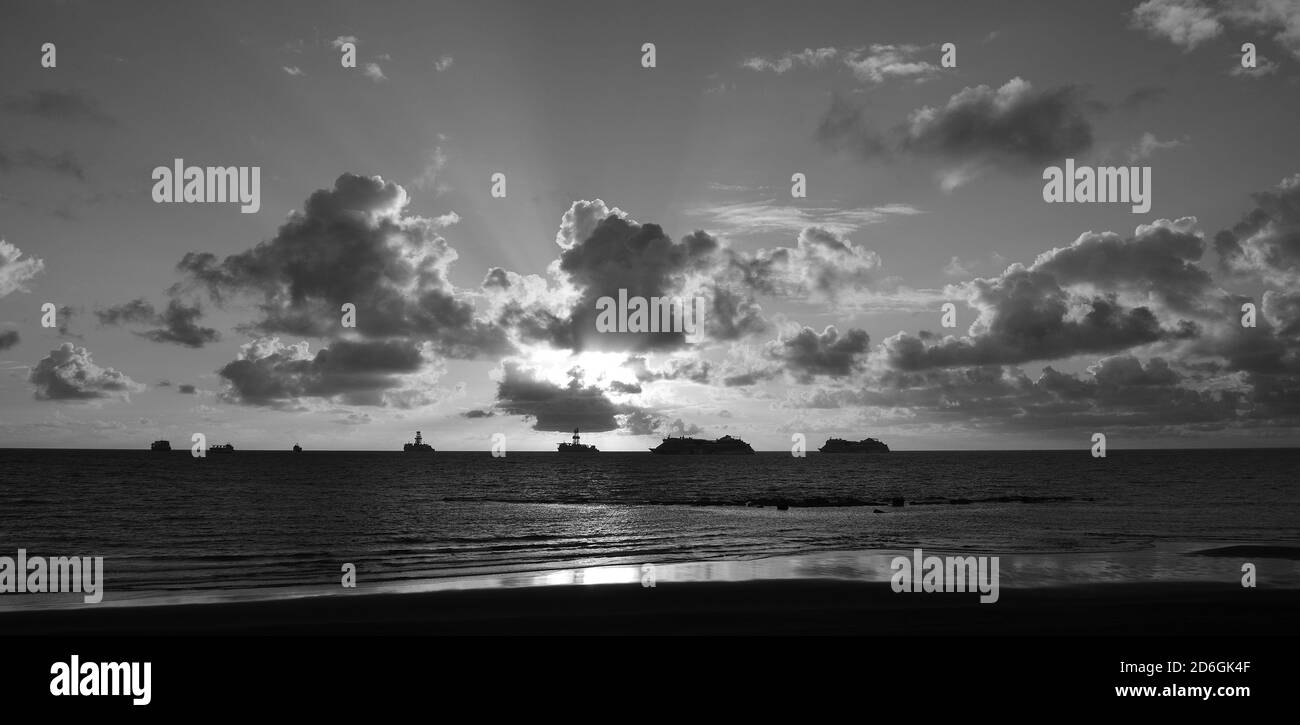 Lever de soleil de la plage avec des navires à l'horizon et ciel avec nuages épars Banque D'Images