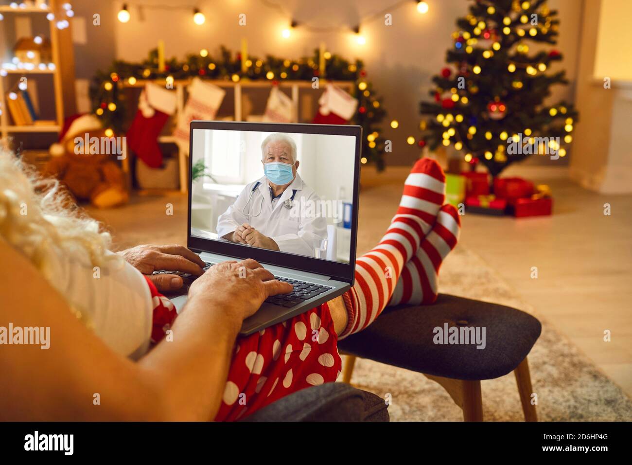 Le Père Noël écoute un médecin dans un masque médical de protection à l'aide d'un appel vidéo. Banque D'Images