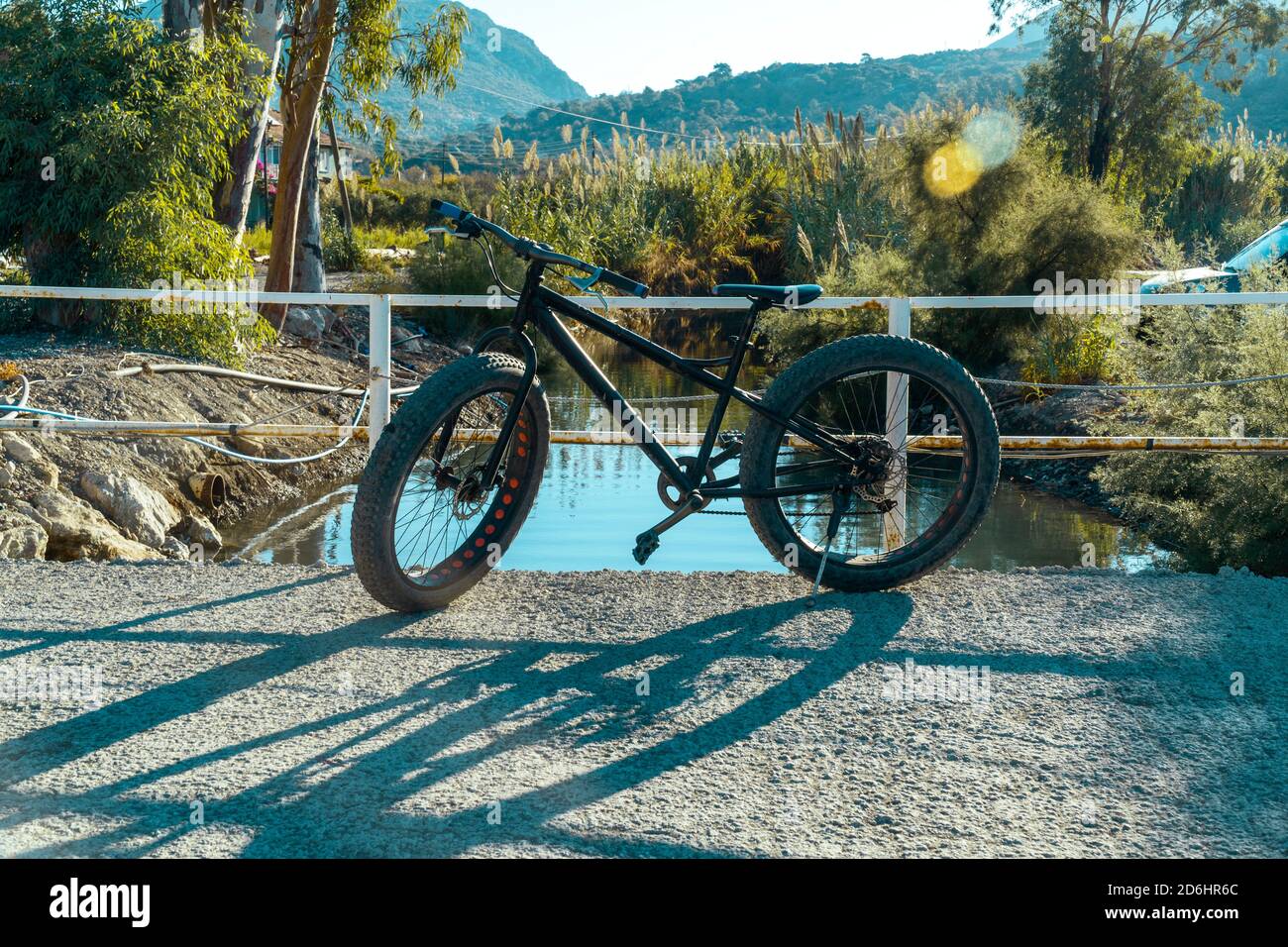 Un nouveau vélo noir pendu au milieu d'un petit pont de rivière par une journée ensoleillée avec une lumière de lentille. L'ombre tombe sur la route. Banque D'Images