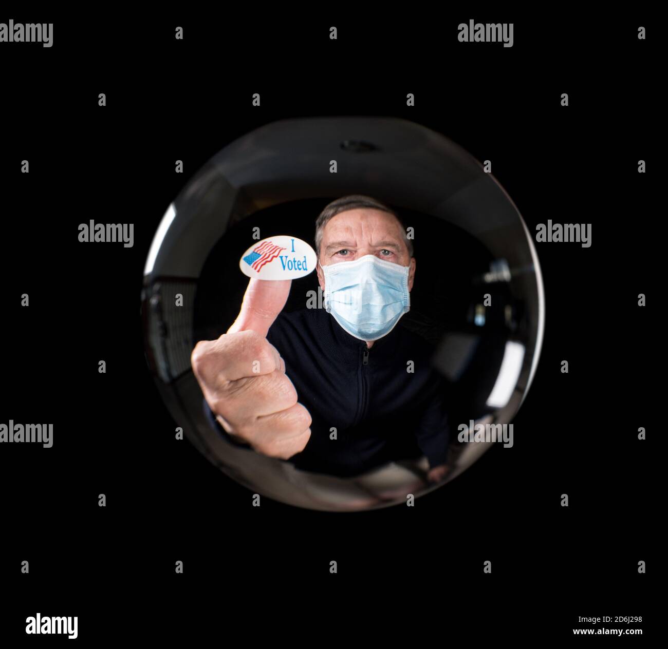 Homme âgé portant un masque facial contre le virus et montrant moi étiquette votée reflétée dans la boule de verre de la chance de dire Banque D'Images