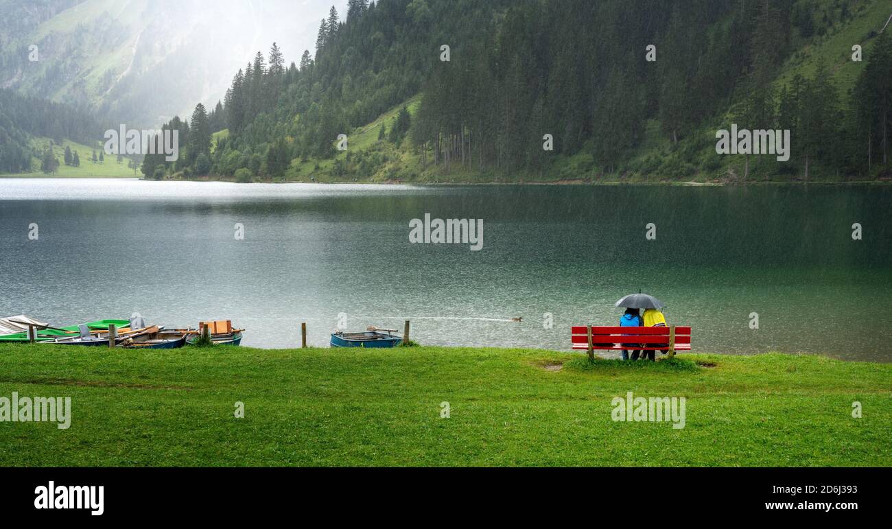 Couple avec parapluie assis dans la pluie à Vilsalpsee dans le Tyrol, Autriche Banque D'Images