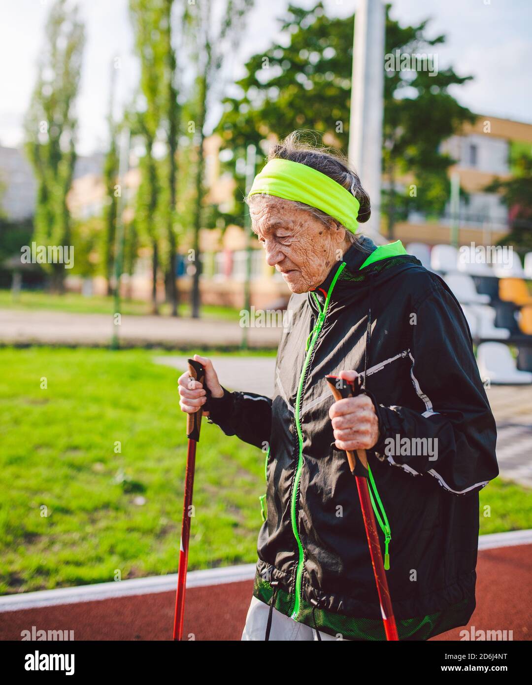 Vieille femme dans les vêtements de sport pratiquant la marche nordique à  l'extérieur sur tapis roulant en caoutchouc dans le stade. Les femmes plus  âgées marchent à pied scandinave utilisent des bâtons
