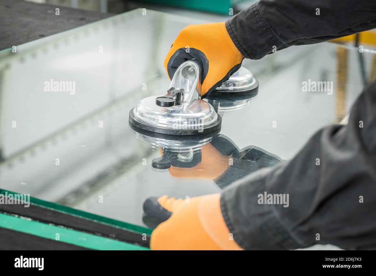 Le Glazier utilise un aspirateur pour les fenêtres. Atelier de fabrication du verre, l'homme lève le panneau de verre épais sur la table à l'aide d'outils spécialisés Banque D'Images