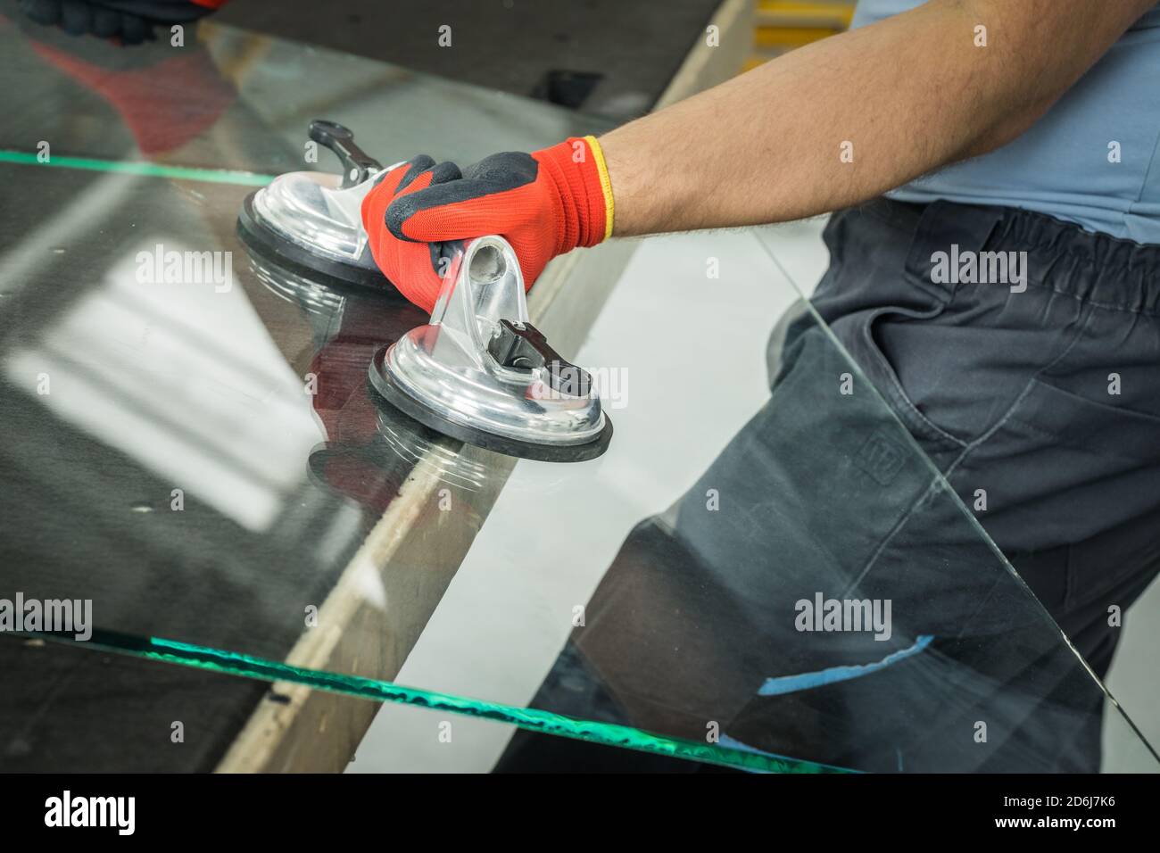 Le Glazier utilise un aspirateur pour les fenêtres. Atelier de fabrication du verre, l'homme lève le panneau de verre épais sur la table à l'aide d'outils spécialisés Banque D'Images