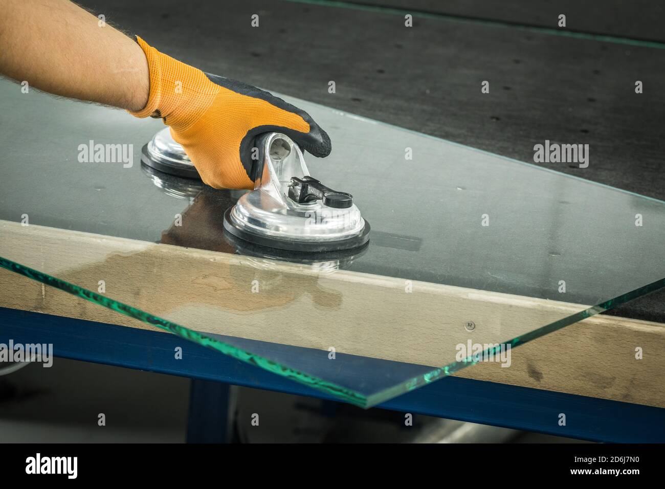 Le Glazier utilise un aspirateur pour les fenêtres. Atelier de fabrication du verre, l'homme lève le panneau de verre épais sur la table à l'aide d'outils spécialisés Banque D'Images