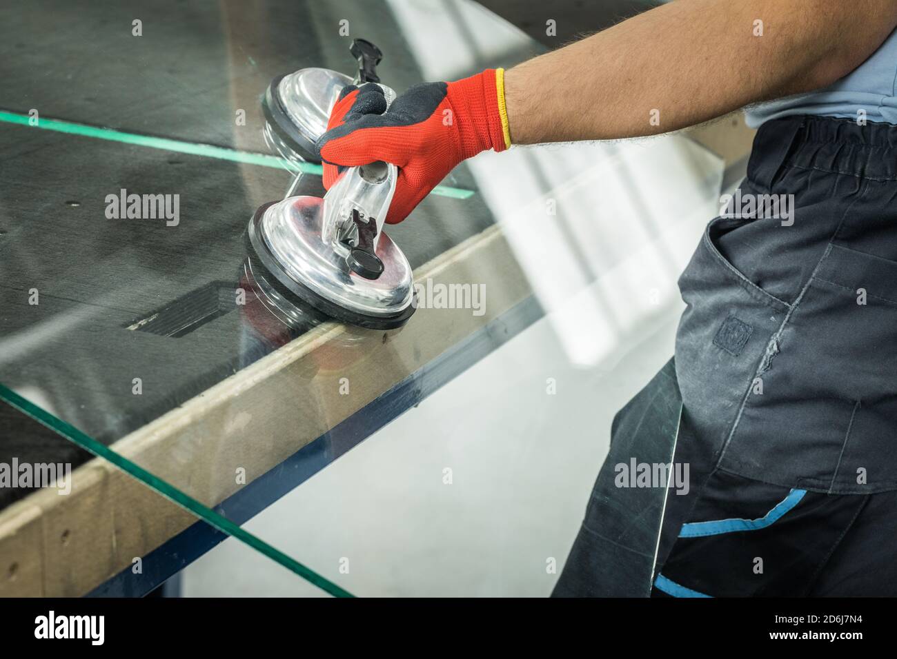 Le Glazier utilise un aspirateur pour les fenêtres. Atelier de fabrication du verre, l'homme lève le panneau de verre épais sur la table à l'aide d'outils spécialisés Banque D'Images