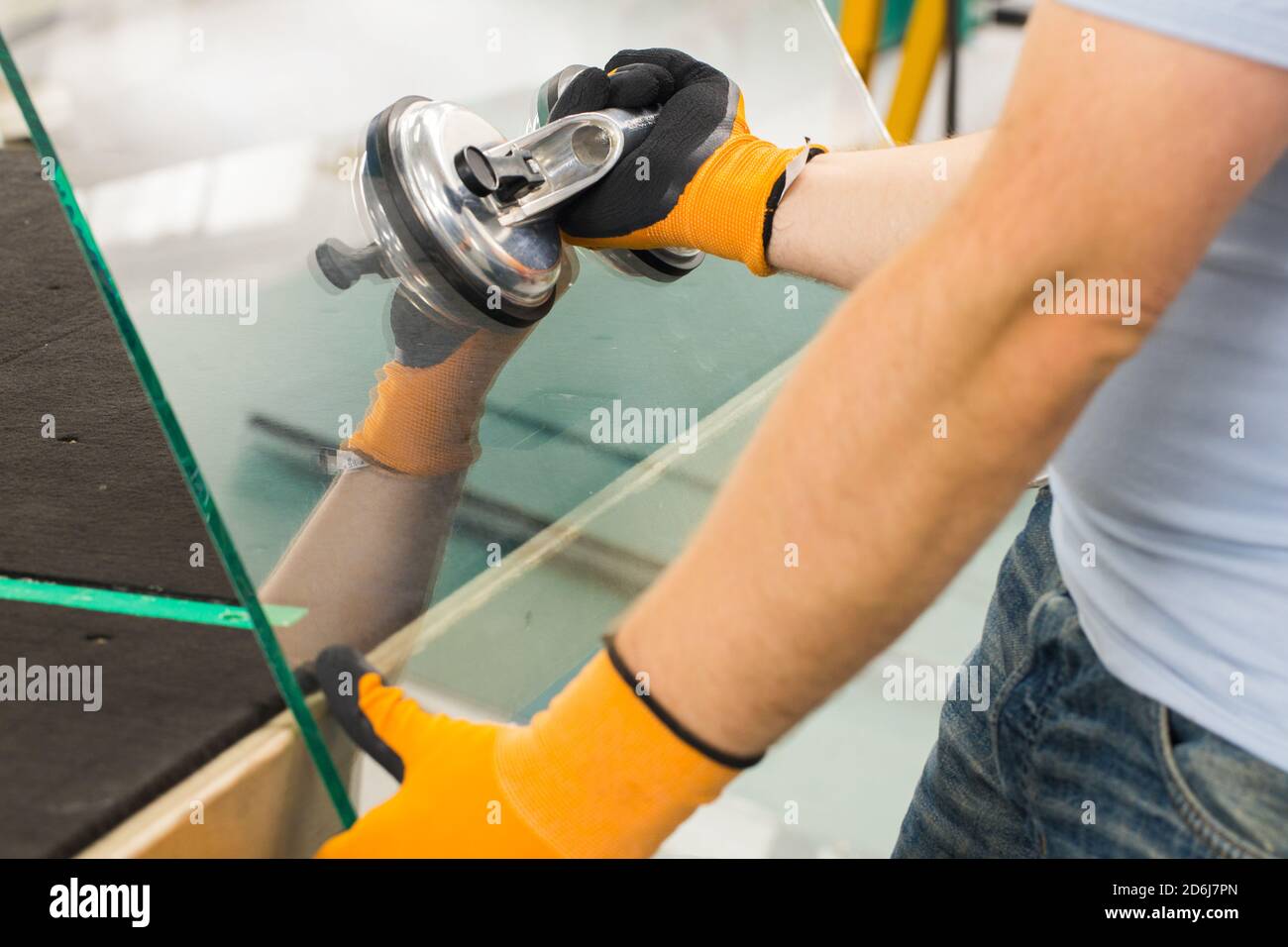 Le Glazier utilise un aspirateur pour les fenêtres. Atelier de fabrication du verre, l'homme lève le panneau de verre épais sur la table à l'aide d'outils spécialisés Banque D'Images