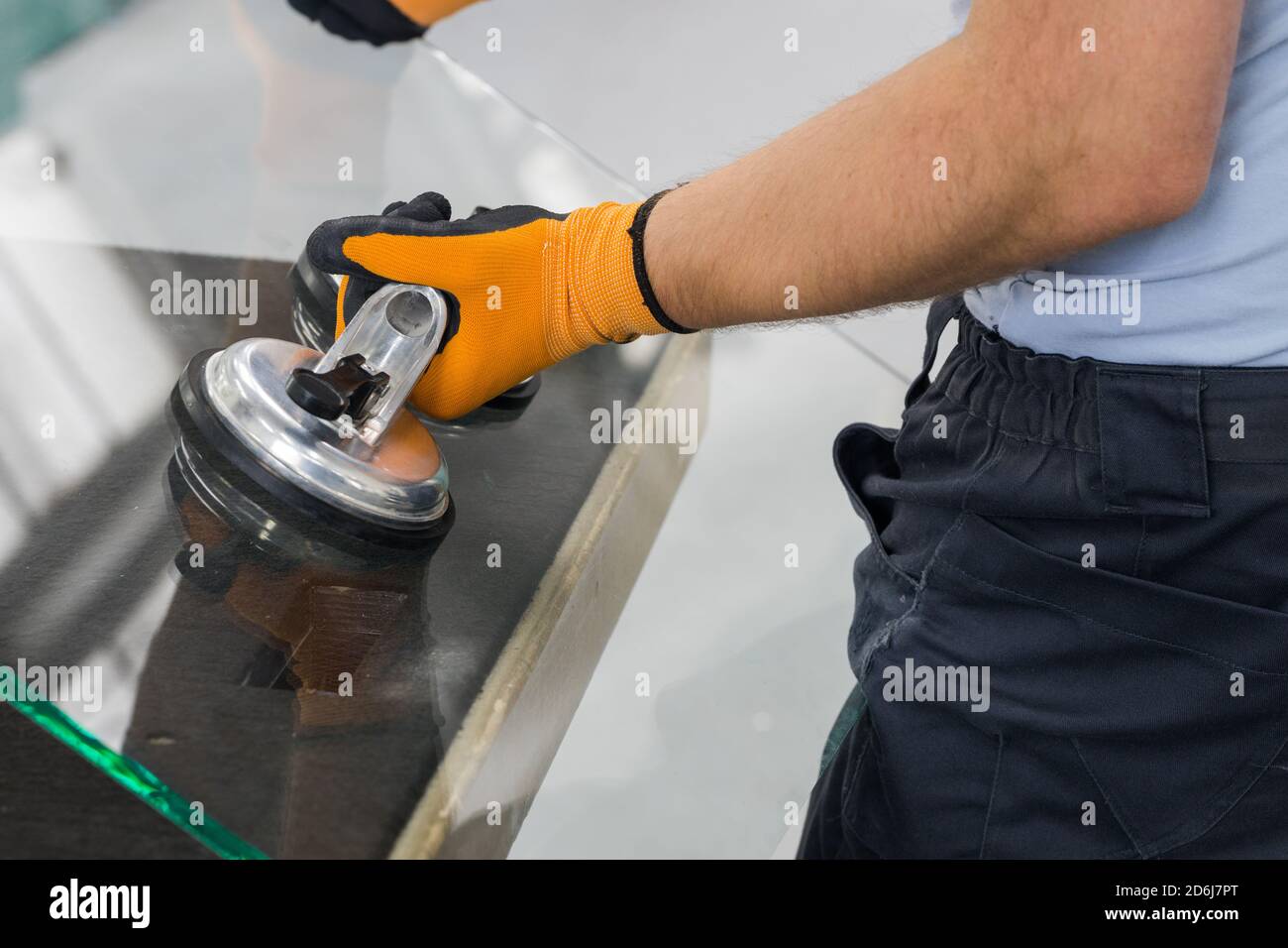 Le Glazier utilise un aspirateur pour les fenêtres. Atelier de fabrication du verre, l'homme lève le panneau de verre épais sur la table à l'aide d'outils spécialisés Banque D'Images