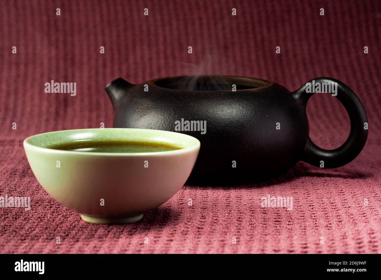 Thé chinois à la vapeur dans un petit thé vert isolé avec un arrière-plan noir et une surface rouge Banque D'Images