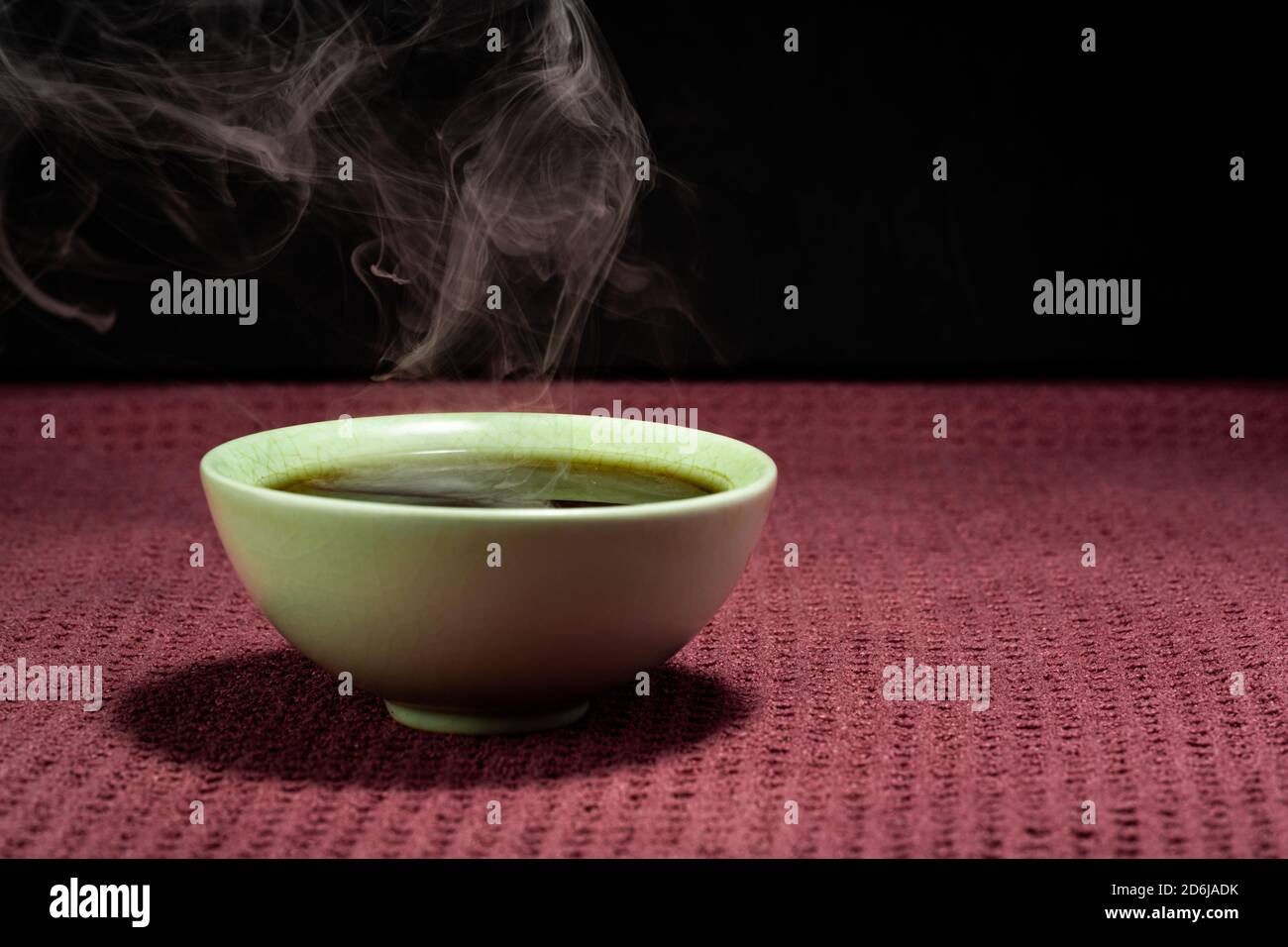 Thé chinois à la vapeur dans un petit thé vert isolé avec un arrière-plan noir et une surface rouge Banque D'Images