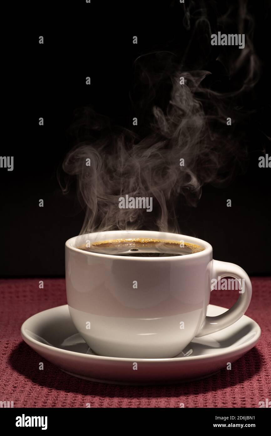 Café cuisant dans une tasse avec soucoupe isolée sur un arrière-plan noir sur une surface rouge Banque D'Images