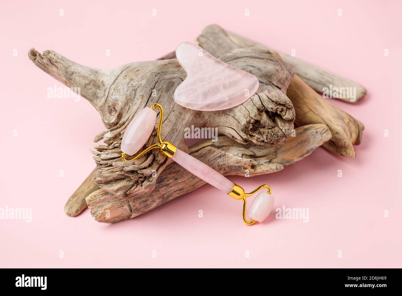 Masseur à quartz rose Gua Sha et rouleau de jade sur fond rose pastel. Pierre de Jade pour le soin du visage et du corps. Pousse horizontale, racine de plante ligneuse, élégant Banque D'Images